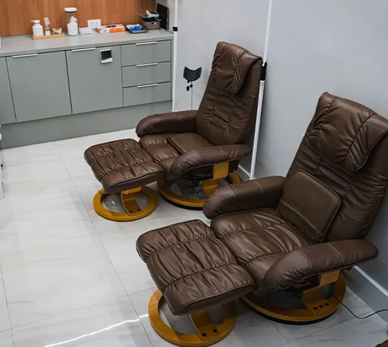 Sala com duas poltronas reclináveis de couro marrom com apoio para os pés, ao lado de um armário de apoio