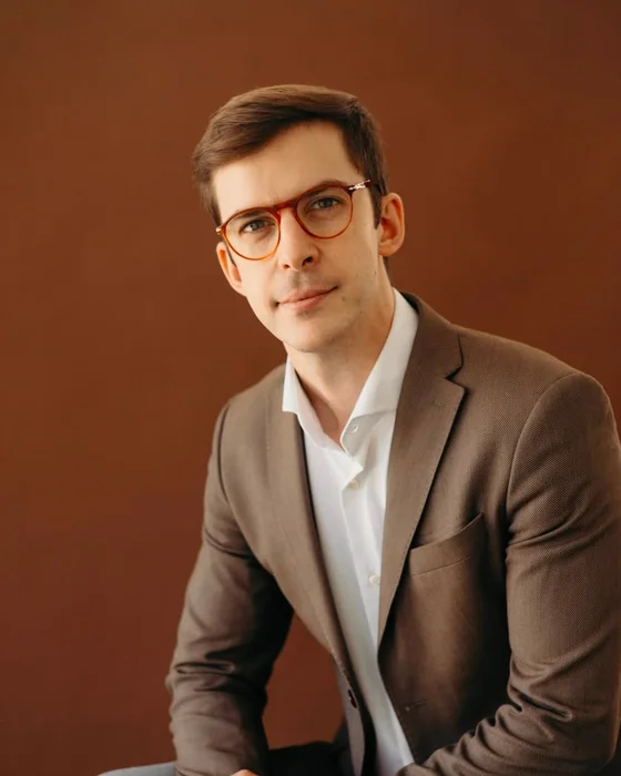 Dr. João Gubert, de blazer e óculos, em fundo de estúdio terracota