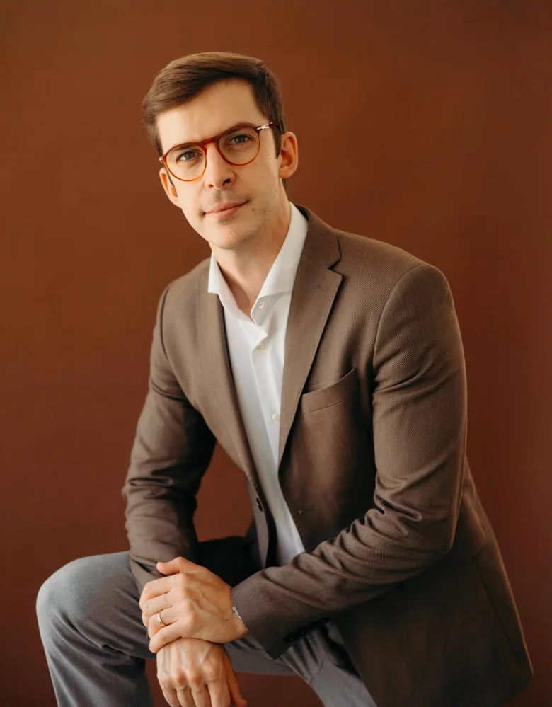 Dr. João Gubert sentado, de blazer, em fundo de estúdio terracota